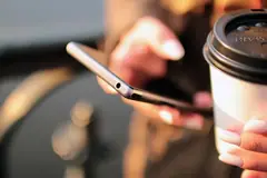 Ръце, които държат смартфон, до чаша кафе